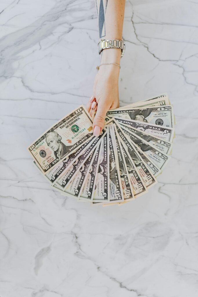 pexels-photo-4968665-4968665 A hand with wristwatch holding a fan of US dollar bills on a marble surface, symbolizing wealth and financial abundance.
